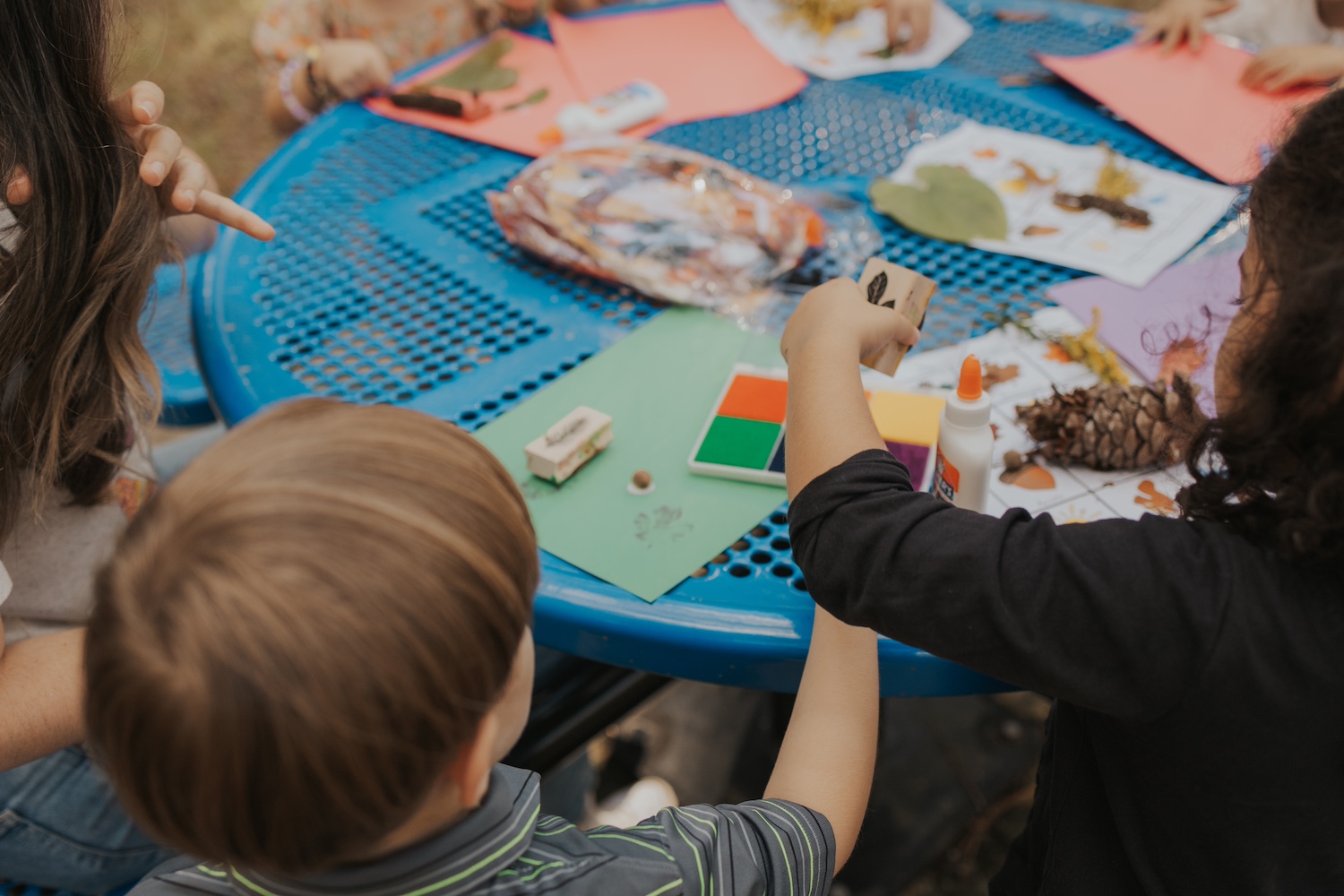 Several children coloring outside on a blue table