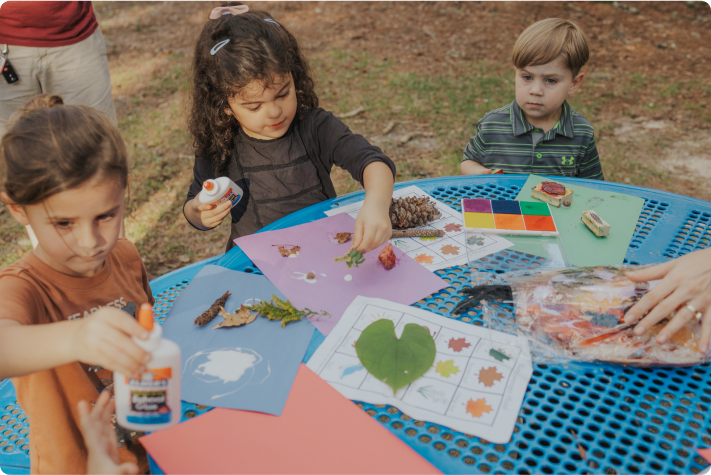 Several children doing a plant activity sitting at a blue table
